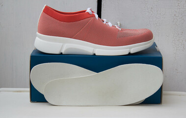 Sport orange shoe with white lacing and orthopedic insoles near the blue box. Treatment and prevention of flat feet and foot diseases.