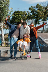 excited multiethnic skaters moving shopping cart with happy woman in skate park.