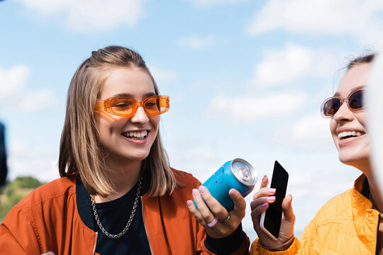 young women with soda can and smartphone with blank screen smiling outdoors.