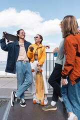 happy asian man holding skateboard near friends with smartphones and soda can. © LIGHTFIELD STUDIOS