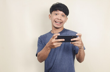 Asian man wearing gray t-shirt with cell phone in hand on isolated background