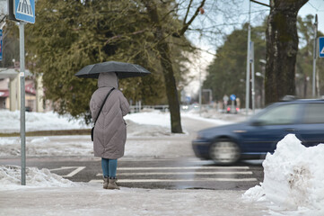 a girl with an umbrella at a pedestrian crossing is waiting for a car to pass by.