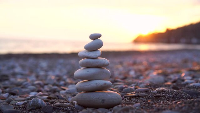 A man's hand makes a pyramid of stones on the beach. Perfect balance of stack of pebbles at seaside towards sunset. Concept of balance, harmony and meditation.