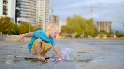 The boy splashes water in the fountain. The baby is wet, but happy. Slow motion