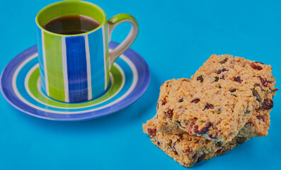 Cranberry granola slices with a cup of coffee on a blue background.