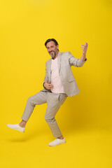 Fototapeta na wymiar Middle aged man pretend playing guitar laughing wearing white suit isolated on yellow background. Handsome mature businessman in white suit. Business concept. Copy space.