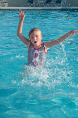 Young girl jumps out of the water in a swimming pool.