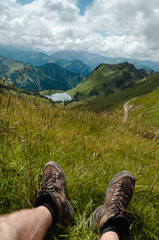 Vertical shot of boots of a male sitting in field with lake Seeaplsee in the distance in Switzerland © Lukas Willke/Wirestock Creators