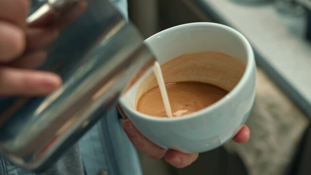 Barista making latte art in specialty coffee shop. Professional man making pouring stream milk with espresso