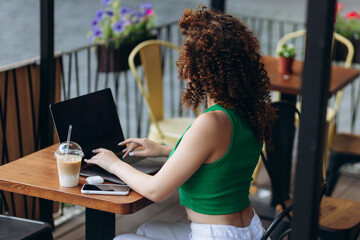 Back view of a curly girl in using laptop in cafe. Student