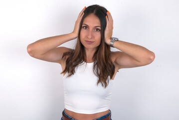 Frustrated young beautiful caucasian woman wearing white top over white background plugging ears with hands does not wanting to listen hard rock, noise or loud music.