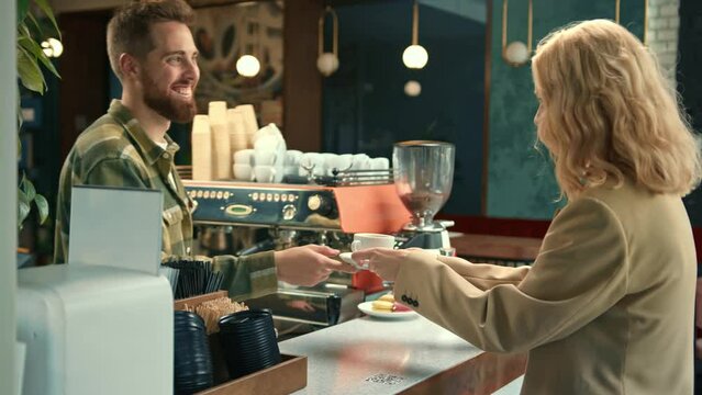 Handsome male barista gives coffee to a girl. Girl buys coffee in a coffee shop.