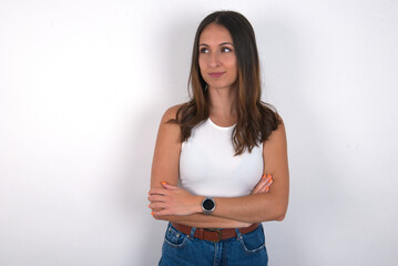 Pleased young beautiful caucasian woman wearing white Top over white background keeps hands crossed over chest looks happily aside