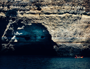 Boat by a rocky cliff with a cave in Algarve, Portugal