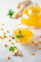 Hot autumn tea with sea buckthorn, ginger and mint in a glass teapot on a gray background