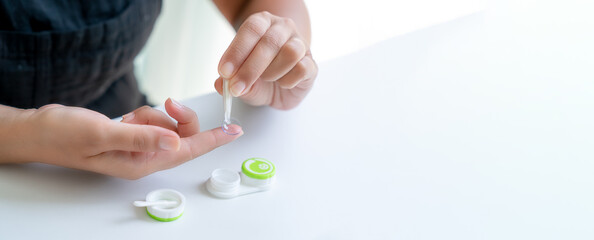 Girl puts contact lens on her index finger with tweezers. There is container for lenses nearby....