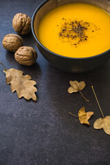 Close-up of delicious creamy homemade pumpkin soup on dark background with walnuts and dry leaves