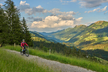 Fototapeta na wymiar pretty senior woman riding her electric mountain bike on the mountains above Oberstaufen with Nagelfluh mountain chain in background, Allgau Alps, Bavaria Germany 