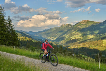 Fototapeta premium pretty senior woman riding her electric mountain bike on the mountains above Oberstaufen with Nagelfluh mountain chain in background, Allgau Alps, Bavaria Germany 
