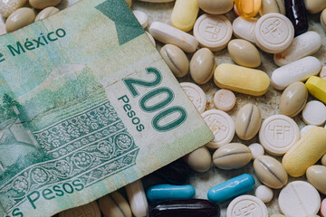 Photo of a Mexican 200 peso bill among pills of many shapes and colors that could probably be used to illustrate the economics of the pharmaceutical industry or drug trafficking in Mexico. - obrazy, fototapety, plakaty