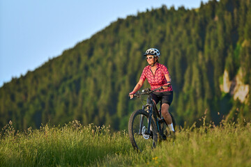 Obraz premium pretty senior woman riding her electric mountain bike on the mountains above Oberstaufen with Nagelfluh mountain chain in background, Allgau Alps, Bavaria Germany