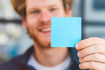 Successful young male businessman or freelancer holding small sheet of paper in his hands close-up, copy space