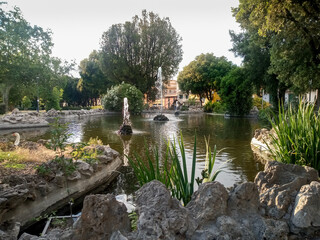 pleasant view of a fountain with 3 water jets in the pond of a park and panorama of the surrounding trees in a peaceful and natural evening atmosphere