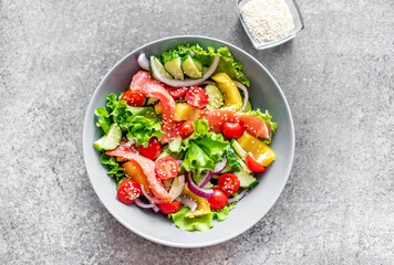Salted salmon salad with fresh green lettuce, cucumbers, tomatoes, sweet peppers and red onions on a stone background. Ketogenic, keto or paleo diet lunch bowl.