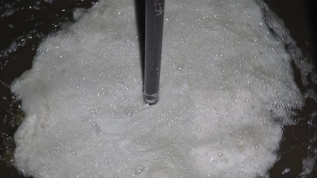 Freshly pressed sunflower oil with white foam rotating in a container. Oily brown liquid after squeezing sunflower seeds or oilseed. Industrial production for oil extrusion. Close up. Slow motion.