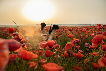 Legs of a girl in high-heeled shoes in a poppy field. Joy and fun concept. Black high-heeled shoes.