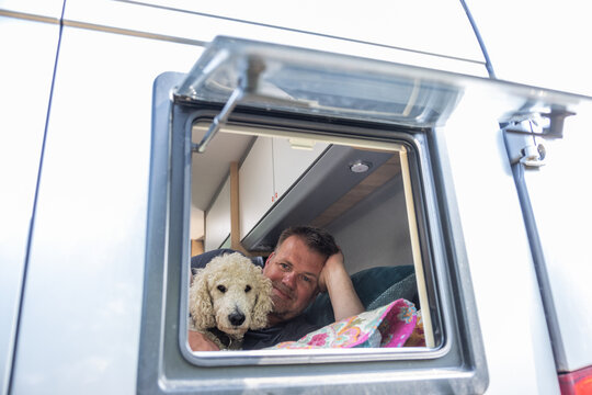 Mann liegt mit seinenem Hund im Wohnmobil auf dem Bett und schaut aus dem Fenster
