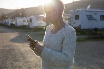 Frau, Camperin, steht auf einem Stellplatz für Wohnmobile und schaut auf ihr Smartphone