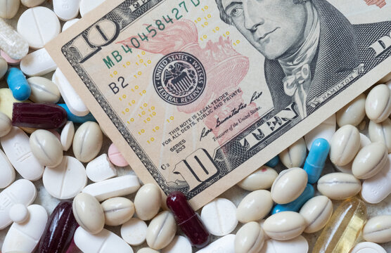 Photo of a US 10 dollar bill among pills of many shapes and colors that could probably be used to illustrate the economics of the pharmaceutical industry in the United States of America.