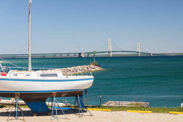 White sailboat with blue stripes in dry dock with Mackinac Bridge in background