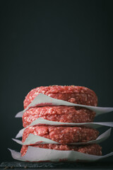 Raw ground beef burger patties separated by parchment paper on a black background