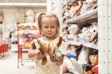 Little caucasian girl choosing a new toy in the big baby store. Big shelfs full of toys