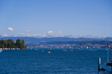 Naklejka premium Scenic landscape with Lake Zürich, leisure boats and Swiss Alps in the background on a sunny summer day seen from City of Zürich. Photo taken June 11th, 2022, Zurich, Switzerland.