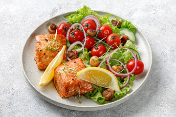Salmon fish fillet and fresh green vegetable salad with lettuce, cherry tomatoes, onion, mushrooms. Close up.