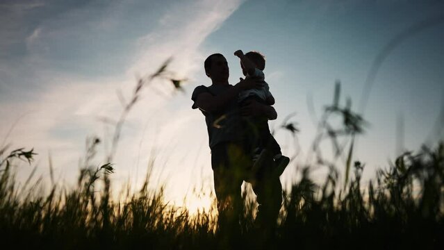 father and son silhouette. happy family kid dream concept. father holding in his arms in the grass in nature at sunset shadow silhouette. fathers day. father and son in the park sunset silhouette