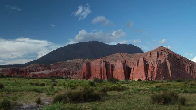 Time lapse in Quebrada de las Conchas in Cafayate, Salta, Argentina. View of the valley grassland, rocky and sandstone mountains under a blue sky with fast white clouds passing by. 