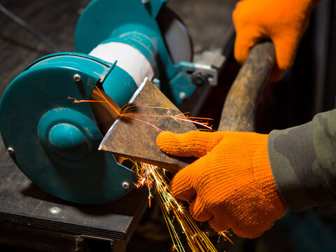 man sharpening an ax blade on a grinder