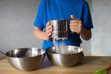 A child prepares dough in metal bowls. Sift the flour. Hands