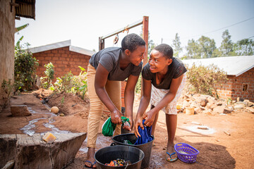 Two african girls wash clothes by hand using soap and a bucket, traditional life in africa.