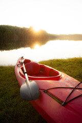 Red kayak with paddle oar on shore of lake at sunset

