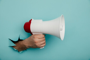 Man's hand arm hold megaphone isolated through torn blue background