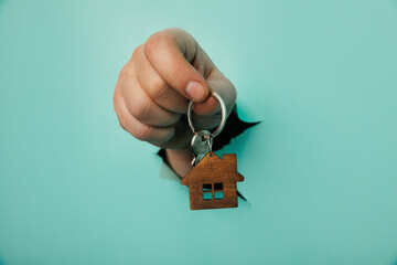 Man's hand with house key through a hole in blue background. House sale and rent concept