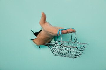 Male hand with shoppind basket on a blue paper background. Sales concept