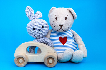 Baby wooden car toy, amigurumi in form of a rabbit and toy bear witn heart embroidered in striped clothes on blue background. Concept of baby toys. 