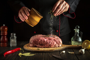 The chef adds spices to raw meat while cooking in the kitchen. Menu concept for hotel