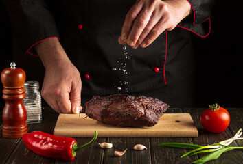 The chef sprinkles the baked beef meat with salt. The concept of cooking delicious food